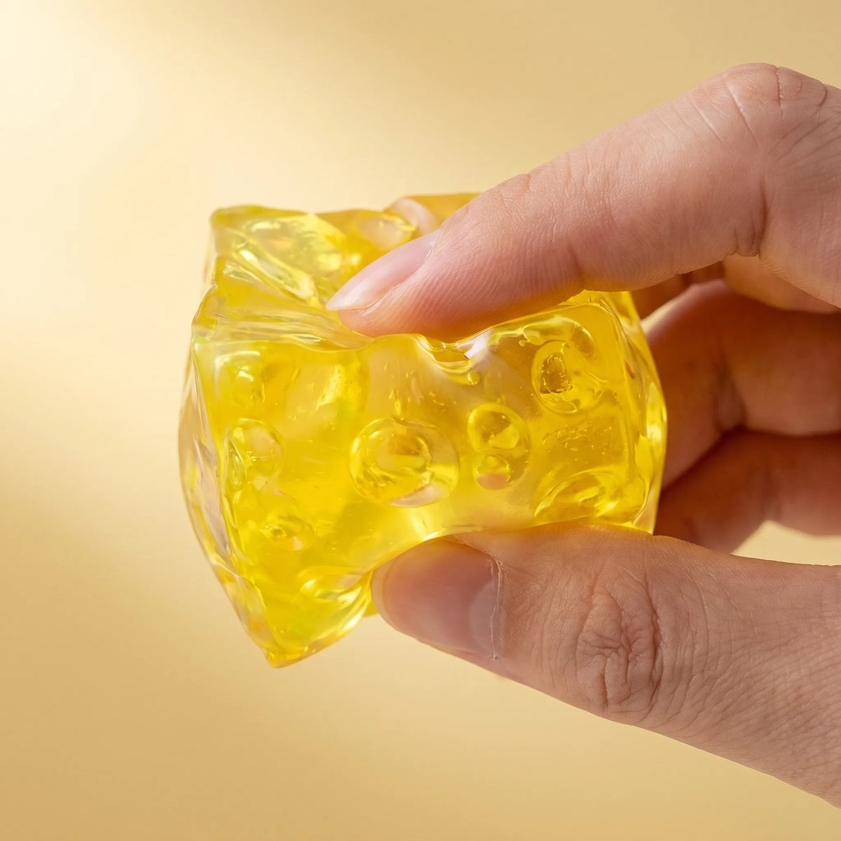Hand squeezing the clear honey yellow cheese squishy block