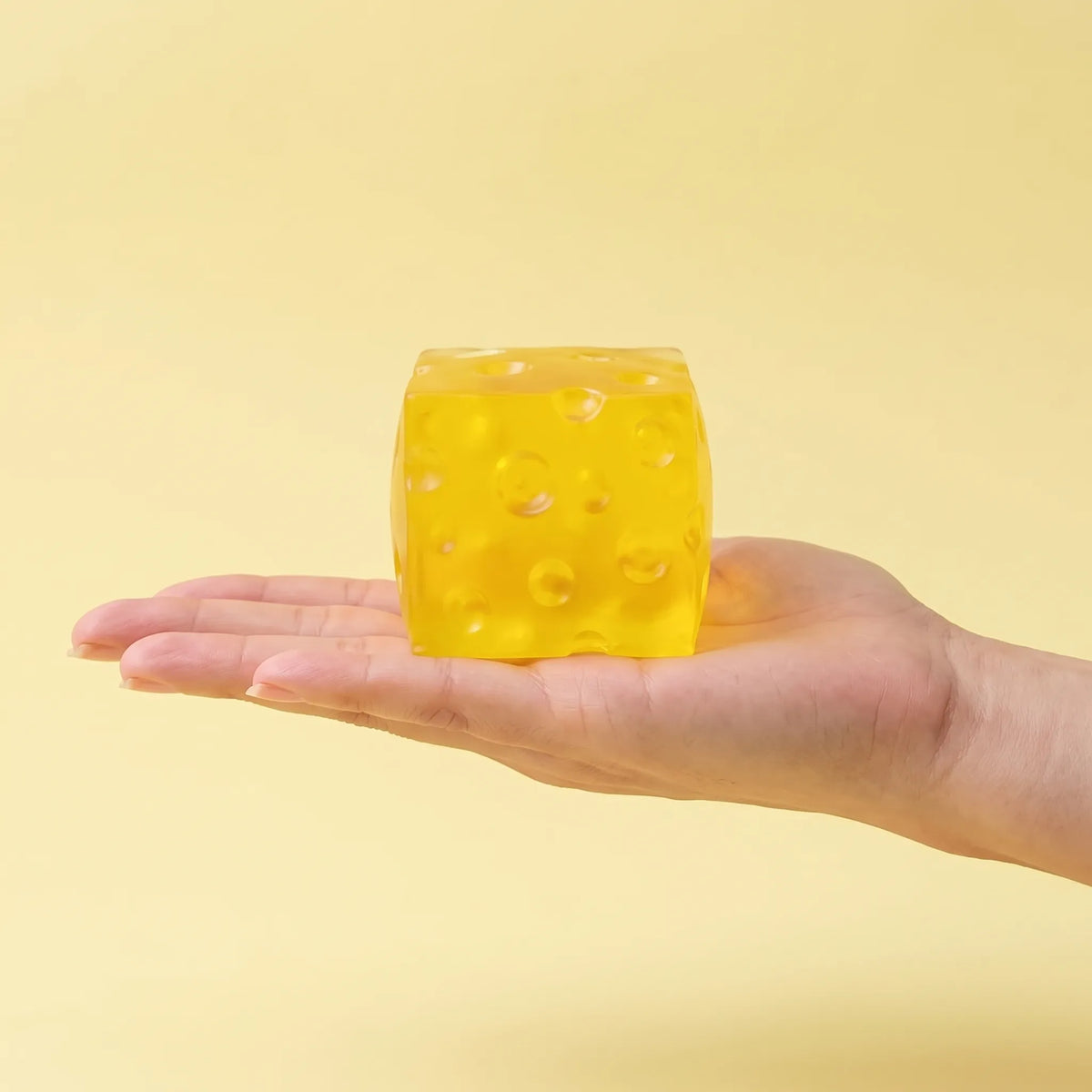 Clear cheese squishy block held between fingers to show its 6 cm size