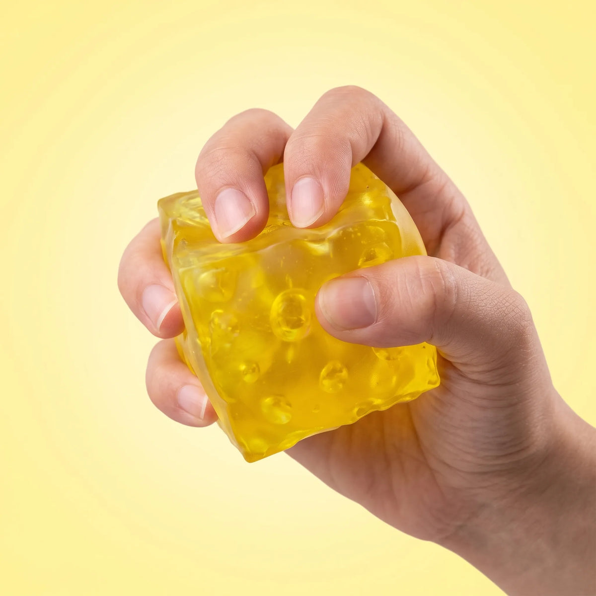 Fingers pinching the translucent cheese squishy block so its holes stretch