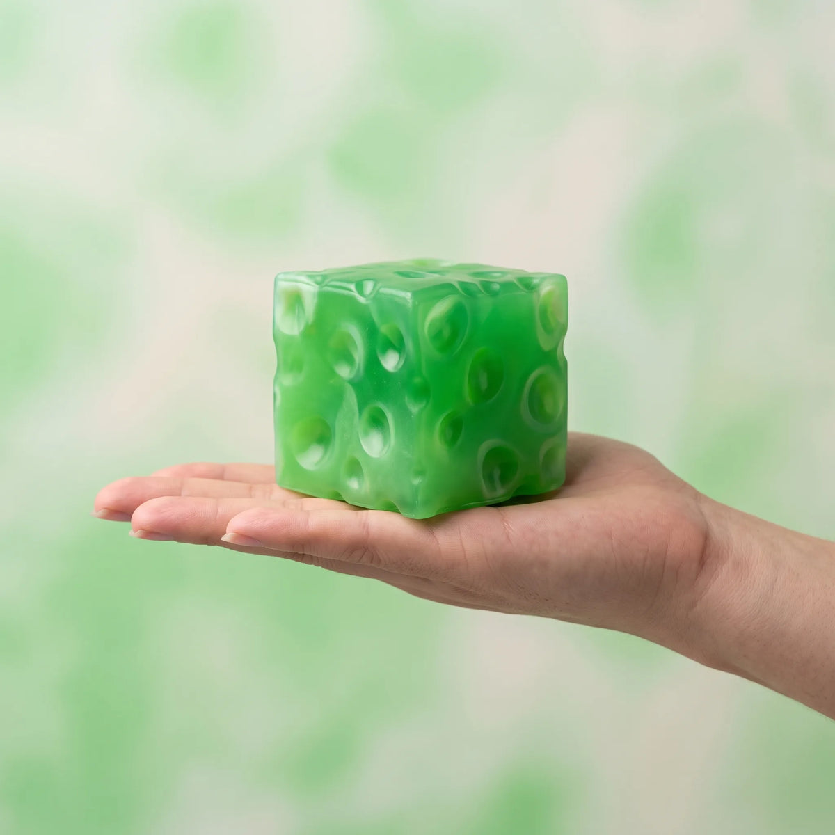 Clear green cheese squishy cube sitting in an open palm