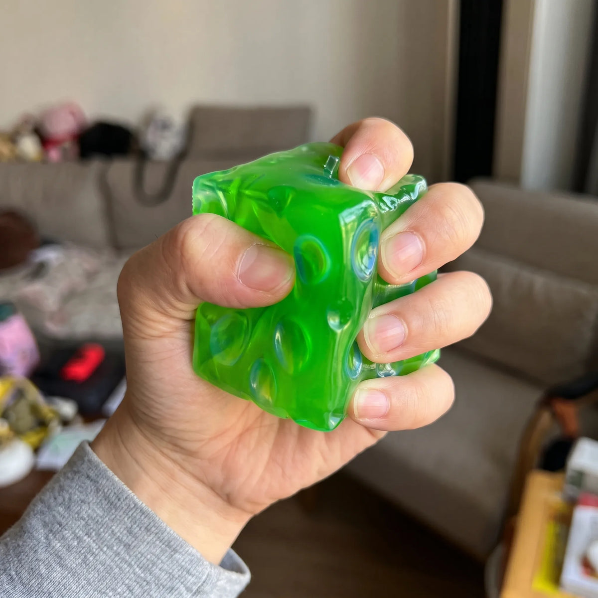 Adult hand pressing the clear green cheese squishy cube flat