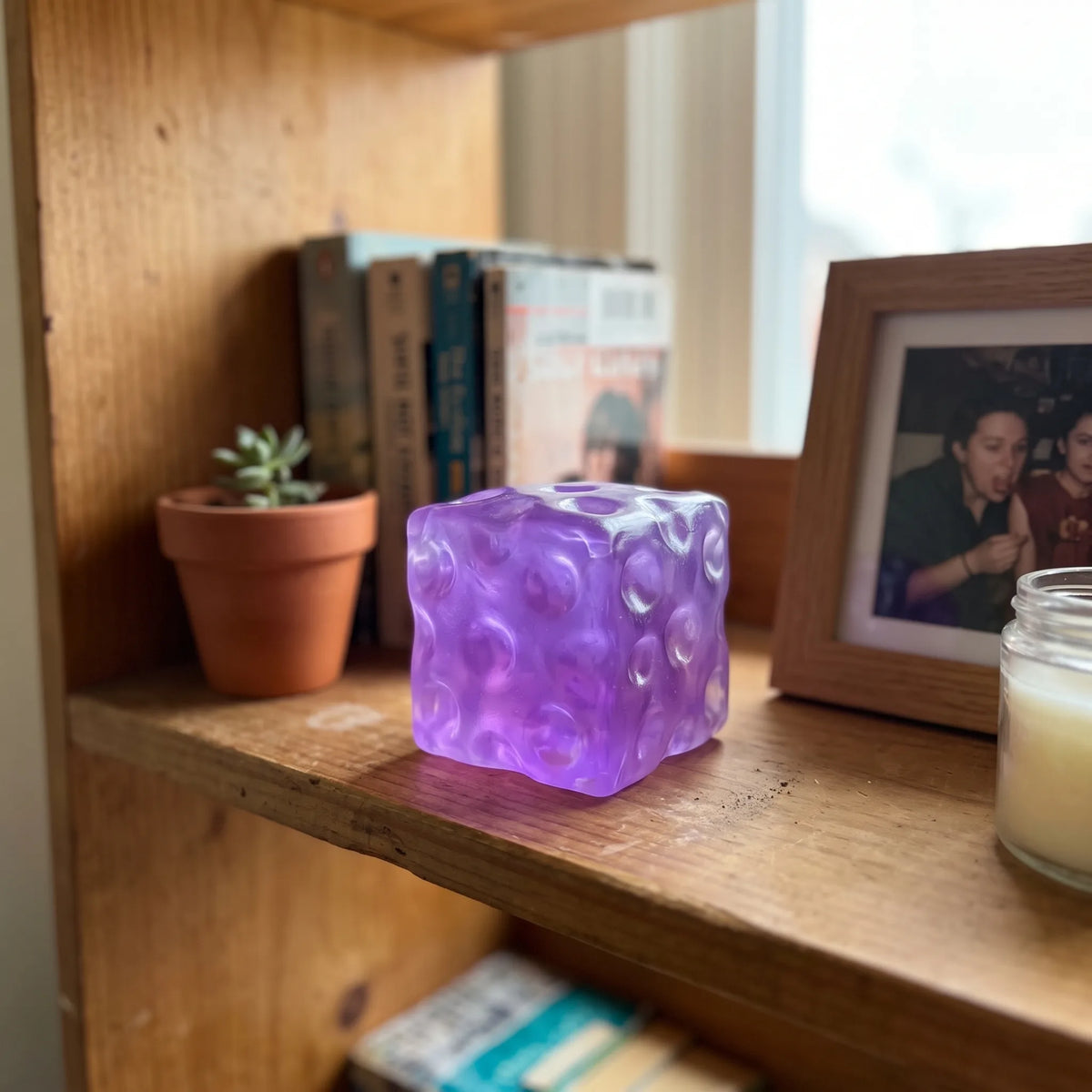 Clear purple cheese squishy cube displayed on a wooden shelf