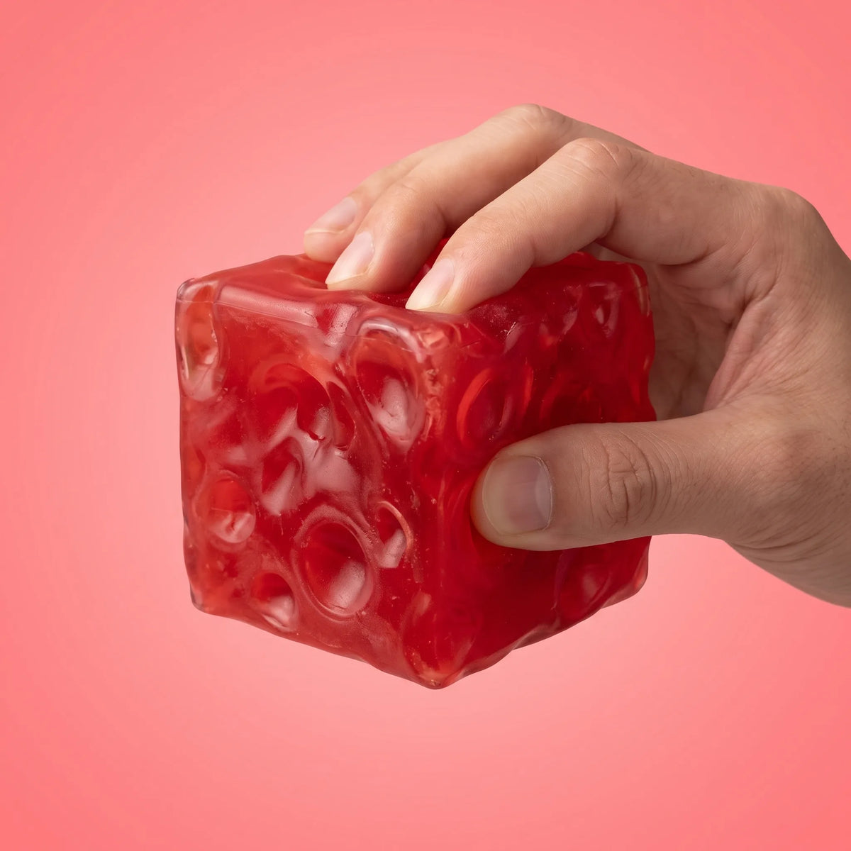 Hand giving the clear red cheese squishy cube a firm squeeze
