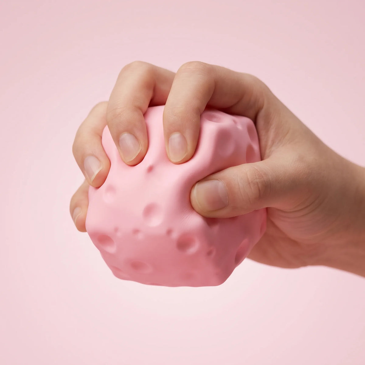 Full fist squeezing the pink cheese squishy block to compress it