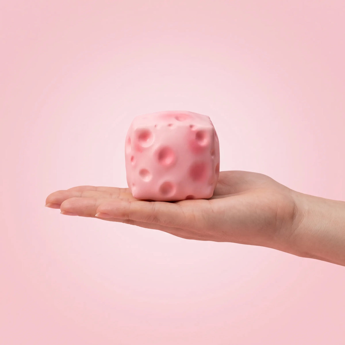 Pink cheese squishy block held in an open hand to show its 6 cm size