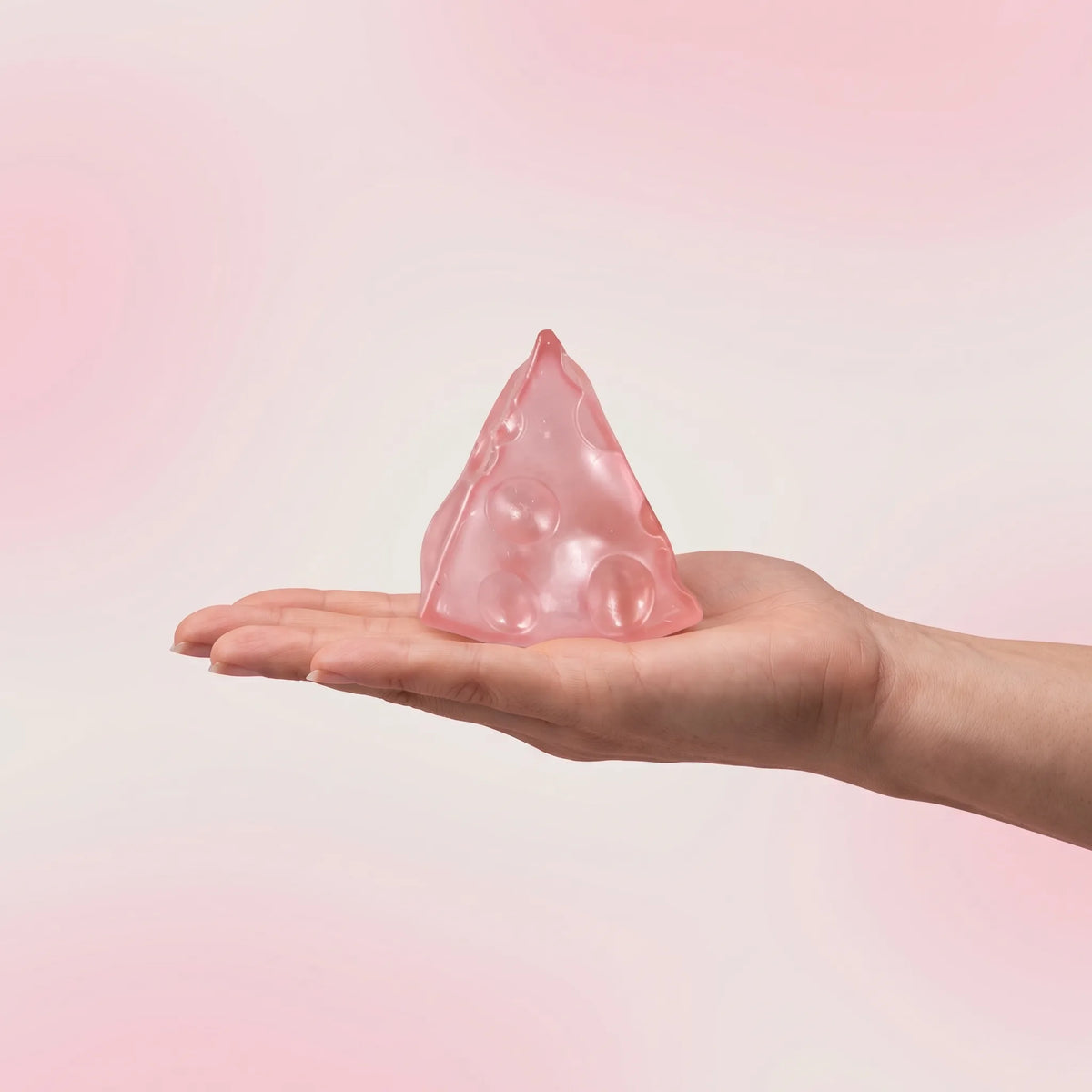 Pink cheese squishy wedge held in an open hand to show its 5 cm size