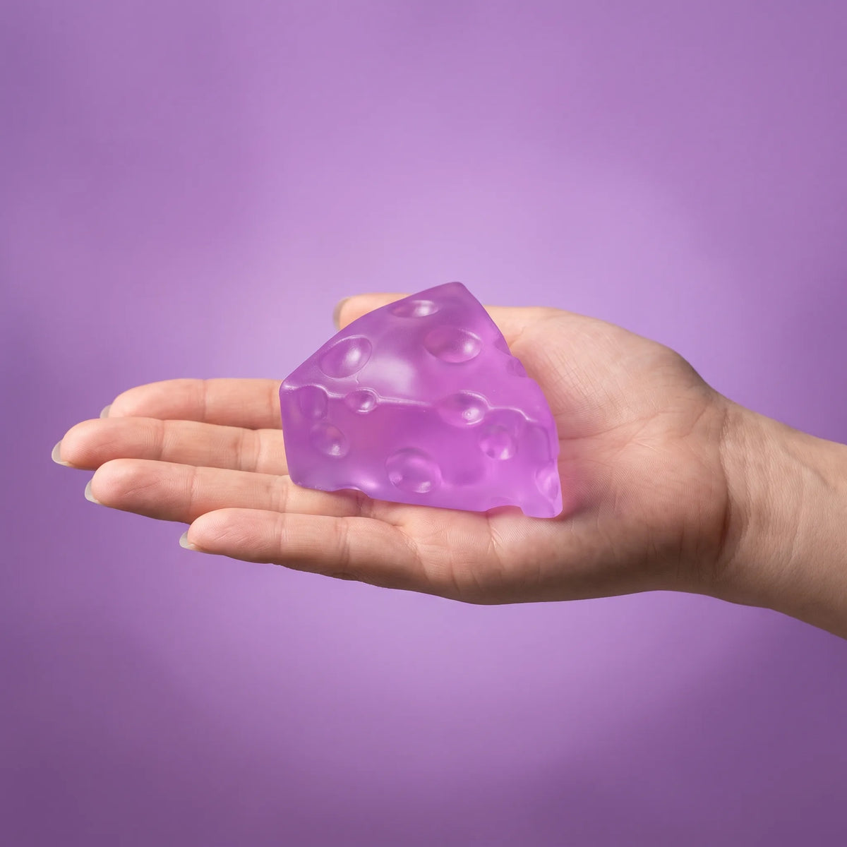 Purple cheese squishy wedge held in an open hand to show its 5 cm size