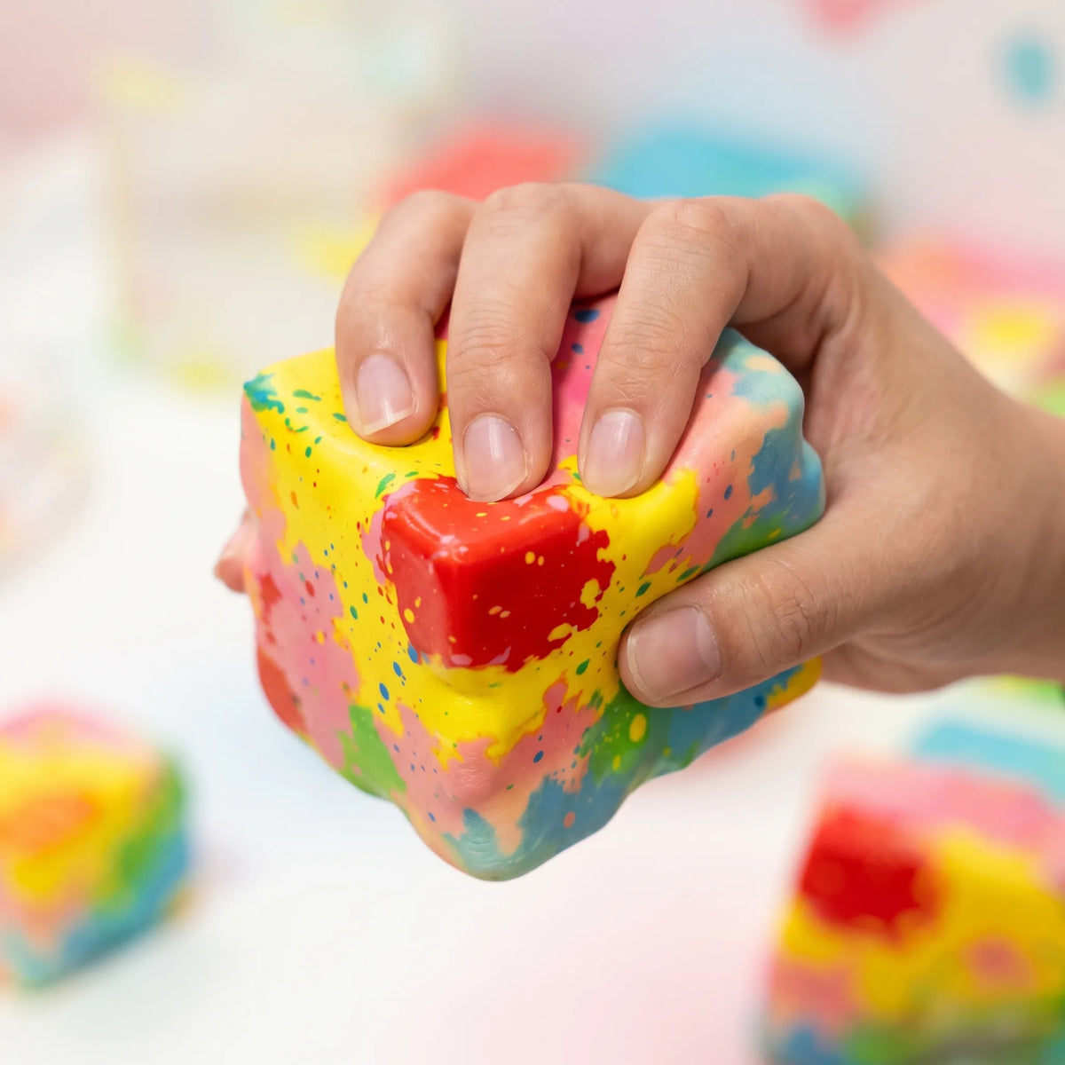 Hand squeezing the paint-splatter cheese squishy block