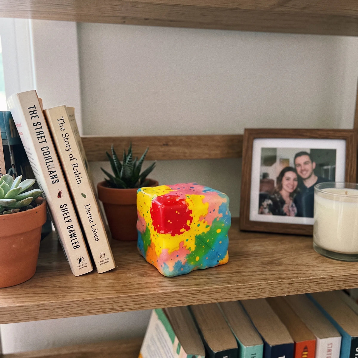 Rainbow paint-splatter cheese squishy block styled in a playful home setting
