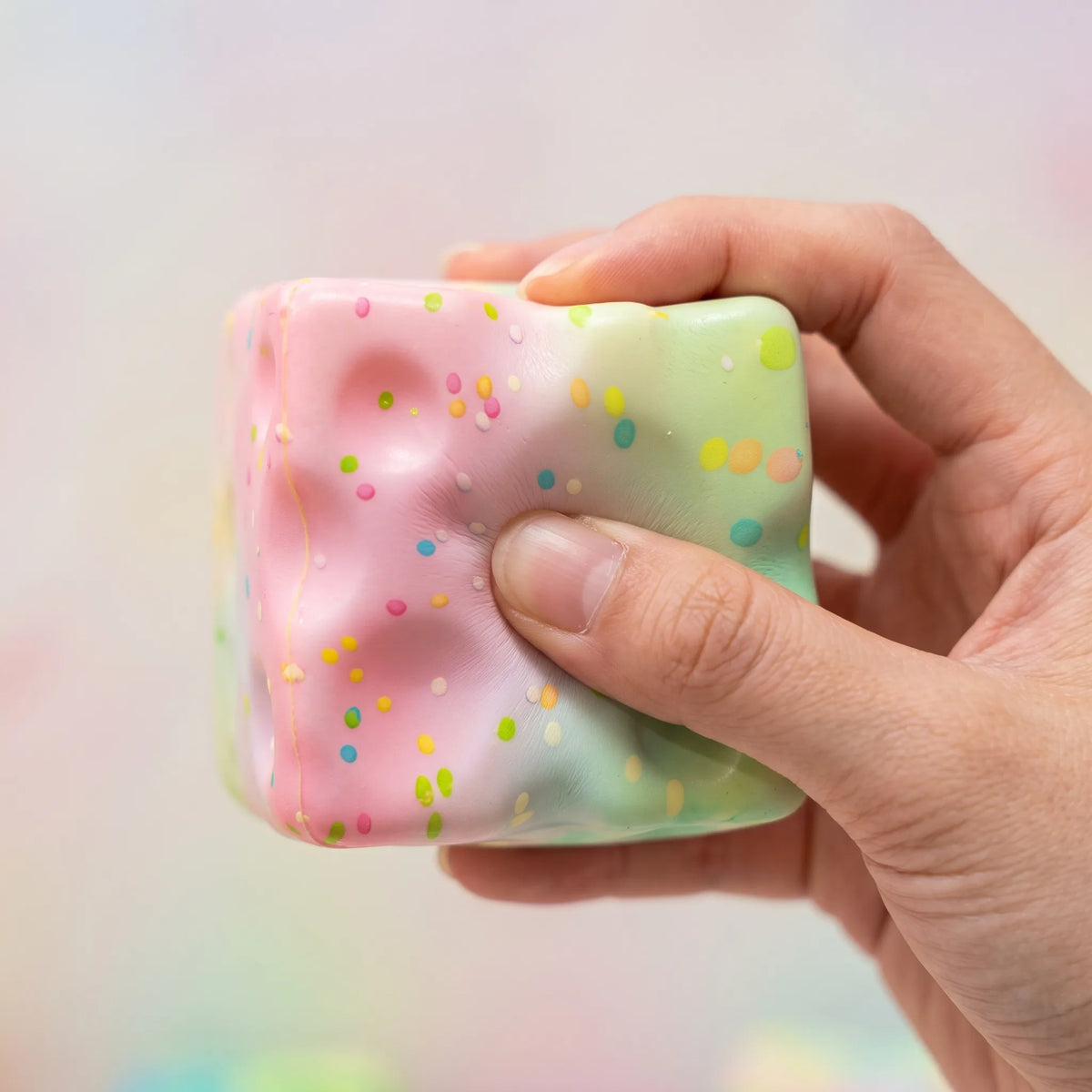 Hand squeezing the pink sprinkle cheese squishy block